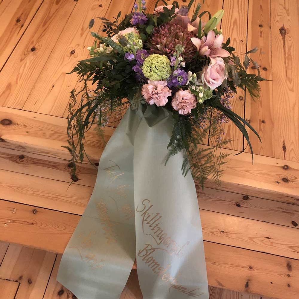 Kistdekoration, rosa och lila blommor, band i grått med text på